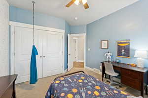 Bedroom with light colored carpet, a closet, a desk, and a ceiling fan