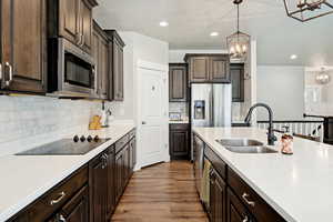 Kitchen with dark brown cabinetry, appliances with stainless steel finishes, decorative light fixtures, light wood finished floors, and tasteful backsplash