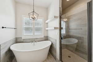 Bathroom with a chandelier, tile walls, a freestanding bath, a shower stall, and a wainscoted wall