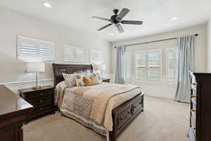 Bedroom with light colored carpet, ceiling fan, recessed lighting, wainscoting, and a decorative wall