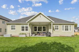 Back of house with a patio, roof with shingles, and a lawn