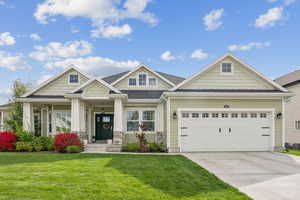 Craftsman-style home with concrete driveway, a front yard, covered porch, stone siding, and an attached garage