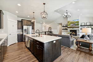 Kitchen featuring dark brown cabinetry, a fireplace, vaulted ceiling, decorative light fixtures, and light wood-style flooring