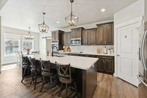 Kitchen with dark brown cabinets, pendant lighting, decorative backsplash, a breakfast bar area, and dark wood finished floors