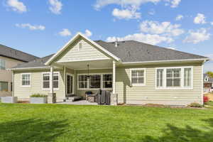 Rear view of property featuring a patio area, a shingled roof, and a lawn