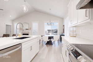 Kitchen with white cabinetry, stainless steel appliances, pendant lighting, range hood, and vaulted ceiling