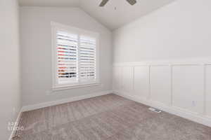 Spare room featuring carpet, vaulted ceiling, a ceiling fan, a wainscoted wall, and a decorative wall