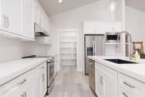 Kitchen featuring decorative backsplash, hanging light fixtures, stainless steel appliances, white cabinetry, and lofted ceiling