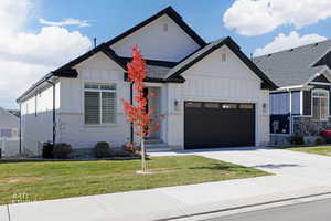 Modern inspired farmhouse with board and batten siding, an attached garage, driveway, and a front yard