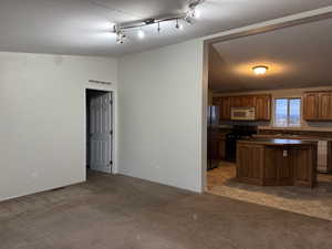 Kitchen with black appliances, light colored carpet, dark countertops, a kitchen island, and lofted ceiling