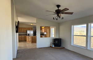 Unfurnished living room featuring a wood stove, vaulted ceiling, ceiling fan, and light carpet