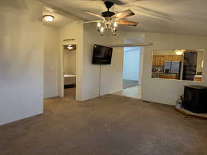 Unfurnished living room featuring ceiling fan, vaulted ceiling, a wood stove, and light colored carpet