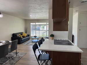 Kitchen featuring a breakfast bar area, a textured ceiling, light wood-style floors, black electric stovetop, and open floor plan