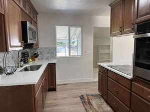 Kitchen with appliances with stainless steel finishes, light wood-style flooring, a textured ceiling, light stone countertops, and backsplash