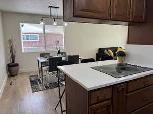 Kitchen with a breakfast bar area, dark brown cabinets, light countertops, light wood-type flooring, and a textured ceiling