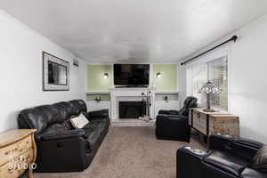 Living area featuring a textured ceiling, a tiled fireplace, carpet, and crown molding