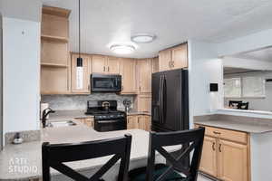 Kitchen with light brown cabinetry, black appliances, a peninsula, decorative backsplash, and pendant lighting