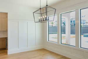 Unfurnished dining area with a decorative wall, light wood-type flooring, wine cooler, and a chandelier