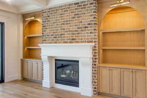 Unfurnished living room featuring built in shelves, light wood finished floors, and a fireplace