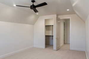 Unfurnished bedroom featuring lofted ceiling, light colored carpet, recessed lighting, a ceiling fan, and a walk in closet