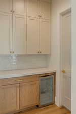 Bar area with wine cooler, light wood finished floors, tasteful backsplash, light stone counters, and brown cabinets