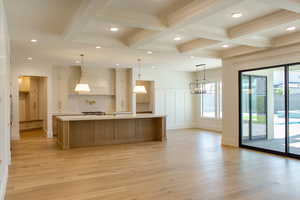 Kitchen featuring a large island with sink, light wood-style floors, pendant lighting, beamed ceiling, and brown cabinetry