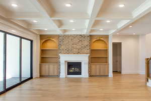 Unfurnished living room featuring beamed ceiling, coffered ceiling, light wood-style floors, a large fireplace, and built in shelves