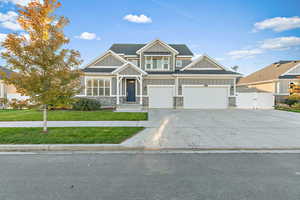 Craftsman house with board and batten siding, driveway, a garage, stone siding, and a gate