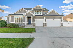 Craftsman-style home with board and batten siding, concrete driveway, a front yard, a shingled roof, and stone siding