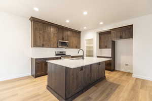 Kitchen with decorative backsplash, dark brown cabinets, appliances with stainless steel finishes, light wood-style floors, and recessed lighting