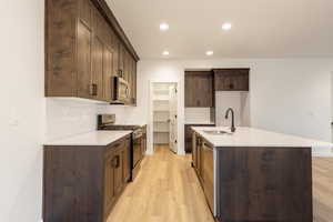 Kitchen featuring tasteful backsplash, appliances with stainless steel finishes, dark brown cabinetry, light stone countertops, and light wood-style floors