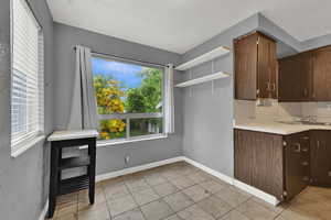 Kitchen with open shelves, light countertops, dark brown cabinetry, and light tile patterned floors