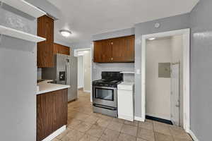 Kitchen with light countertops, appliances with stainless steel finishes, light tile patterned floors, open shelves, and electric panel