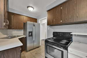 Kitchen featuring stainless steel appliances, light countertops, light tile patterned flooring, a textured ceiling, and dark brown cabinets