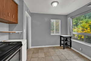 Kitchen featuring light countertops, light tile patterned flooring, brown cabinets, a textured wall, and stainless steel electric stove