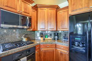 Kitchen featuring black appliances, tile countertops, backsplash, and brown cabinetry