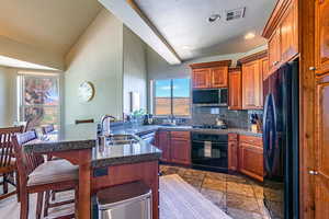 Kitchen featuring a breakfast bar area, brown cabinetry, black appliances, a peninsula, and backsplash