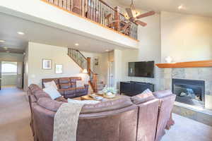 Living room featuring a towering ceiling, recessed lighting, a tile fireplace, carpet floors, and stairs