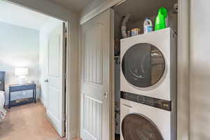 Laundry area featuring estacked washer and dryer and light colored carpet