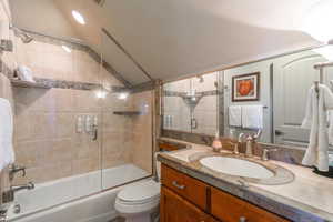 Full bath with enclosed tub / shower combo, lofted ceiling, and vanity