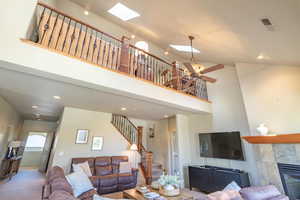Living area with a towering ceiling, recessed lighting, a fireplace, a skylight, and stairs