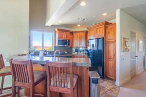 Kitchen with a peninsula, brown cabinetry, black fridge with ice dispenser, a kitchen breakfast bar, and backsplash
