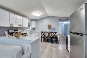 Kitchen with appliances with stainless steel finishes, light wood-style floors, a peninsula, white cabinetry, and vaulted ceiling
