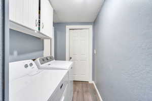 Washroom with cabinet space, a textured ceiling, a textured wall, dark wood-style flooring, and washing machine and dryer