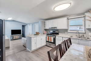 Kitchen with stainless steel appliances, a peninsula, lofted ceiling, light wood-style flooring, and white cabinetry