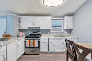 Kitchen with gas range, open shelves, white cabinetry, and light wood-style floors