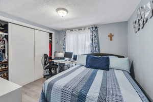 Bedroom featuring a closet, light wood-style flooring, a desk, and a textured ceiling