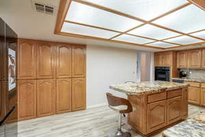Kitchen with a center island, brown cabinetry, oven, light wood-style floors, and fridge