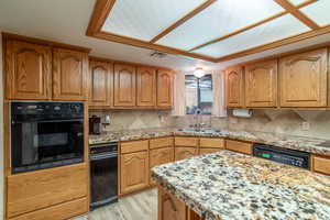 Kitchen featuring brown cabinets, black appliances, light stone countertops, light wood-type flooring, and backsplash
