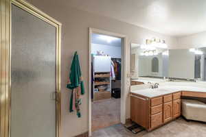 Bathroom featuring vanity, a walk in closet, a shower stall, a textured ceiling, and light tile patterned floors